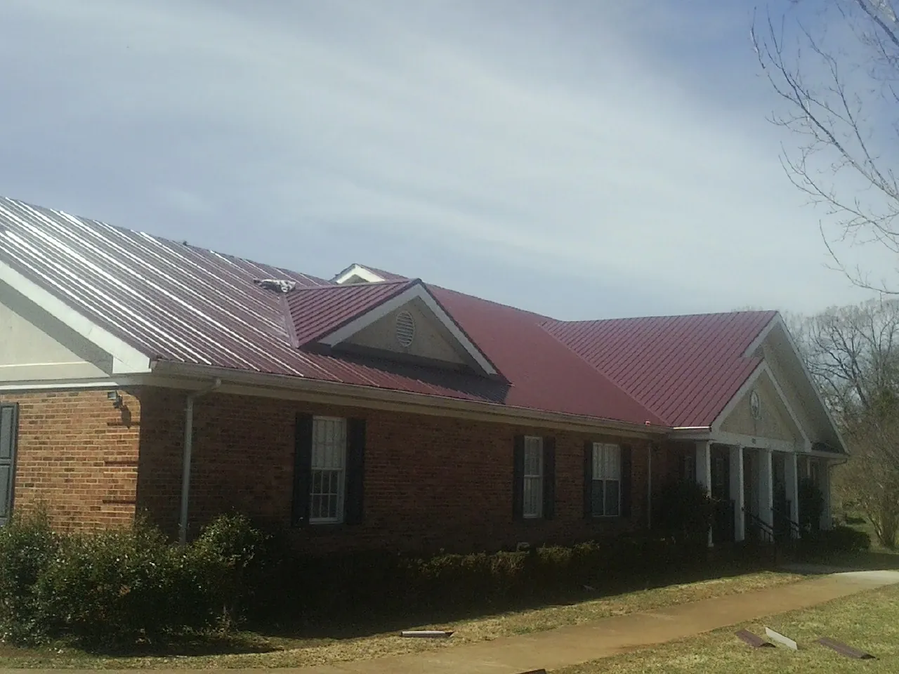 Red metal roof with gabled entries on a long brick building, from a Hail Damage Roof Repair job in Snyder
