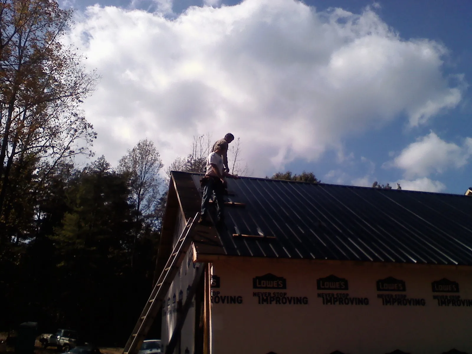 Roofer fastening dark metal panels high against a cloudy sky, from a Roof Inspection job in Snyder