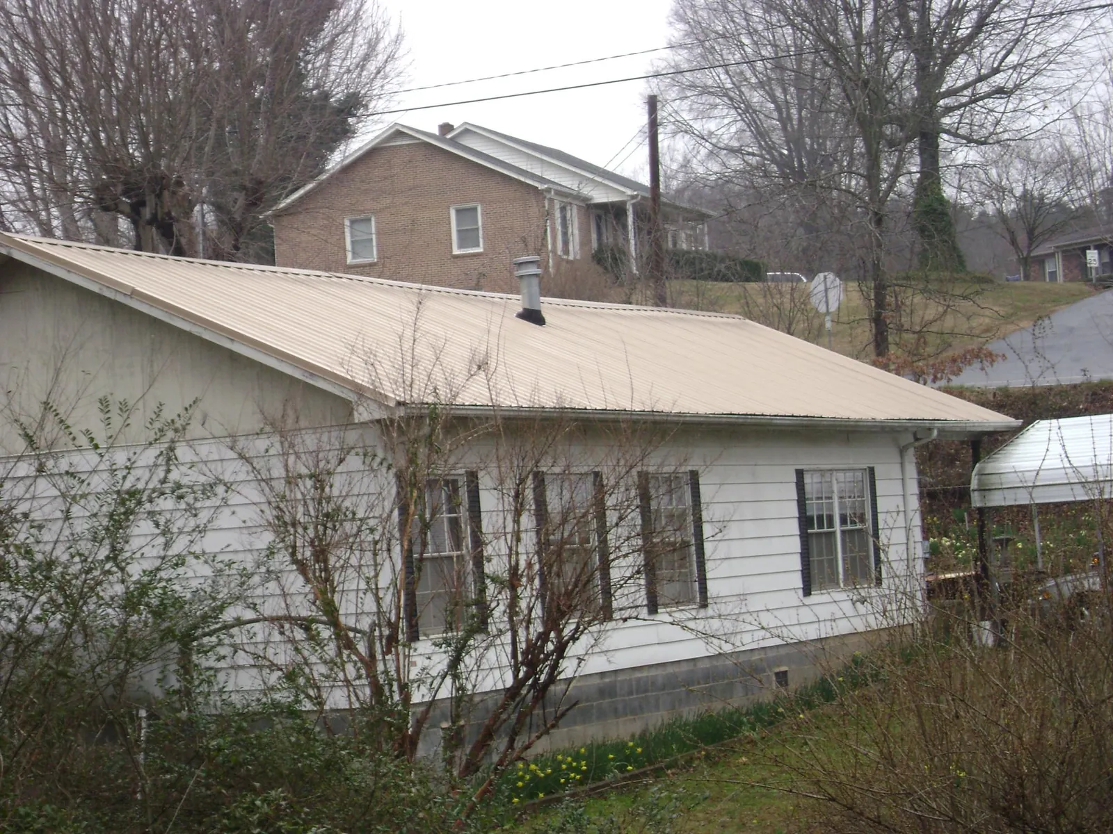 Tan metal roof on a white sided house set into a hillside — Commercial Roofing by Roofing Brothers in Snyder